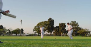 Antrenman seansını başlatan çeşitli erkek takım arkadaşları bovling oynayıp kriket sahasında kırmızı topu yakalıyorlar. Spor, takım çalışması, atletizm, açık hava, eğlence, aktivite, rekabet