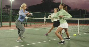 Tenis koçu, çömelmiş öğrencileri yönetiyor hamlelerini yapıyor, kıvırıyor, akşam karanlığında kortta ağla ısınıyor. Atletizm, antrenman, spor, spor, takım çalışması, egzersiz