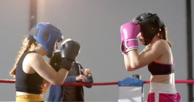 Dişi boksörler ringde yumruk tokuşturuyor, mavi kulaklıklı sporcu vücut atışı yapıyor, hakem durduruyor. Atletizm, dövüş, güç, kararlılık, rekabet, fitness, eylem