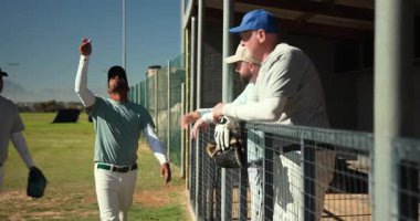 Yürüyen Afrikalı Amerikalı oyuncu beyzbolu yedek kulübesinde oynuyor, koçuna beşlik çakıyor. Atletizm, takım ruhu, sportmenlik, rahatlık, yoldaşlık, açık hava, canlı