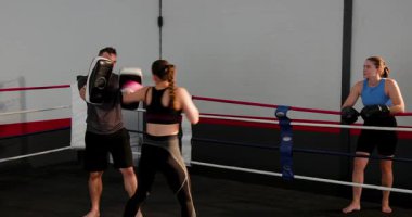 Erkek antrenör kanca için eldiven değiştiriyor, kadın stajyer eldiven takıyor ve yüzüğe yumruk atıyor. Eğitim, uygunluk, kardiyo, spor, disiplin, kararlılık, motivasyon