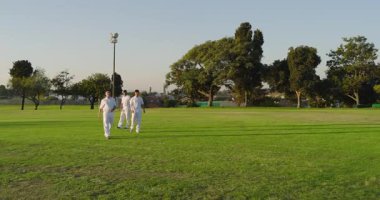 Çeşitli kriket takım arkadaşları, kızılderili bovling oyuncusuna parkta topçu olarak kırmızı topu veriyor. Atletik, takım çalışması, eğlence, açık hava, spor, rekabet, dinamik
