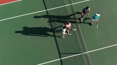 Tenis takımından çeşitli takım arkadaşları sahadan çıkarken raketlerle tokalaşıyor. Tenis, sportmenlik, takım çalışması, açık hava, aktif, rekabet, eğlence