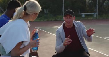 Koç yedek kulübesinde bilekleri kontrol ediyor ve çeşitli stajyerlere tenis kortunda antrenmanlarına devam etmeleri için işaret veriyor. Sporcular, akıl hocalığı, takım çalışması, motivasyon, eğitim, açık hava, enerjik