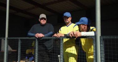 Erkek antrenör ve oyuncular yedek kulübesindeki tel örgülerle birbirlerine yumruk tokuşturuyorlar. Atletizm, takım çalışması, yoldaşlık, spor, aktivite, günlük, açık hava