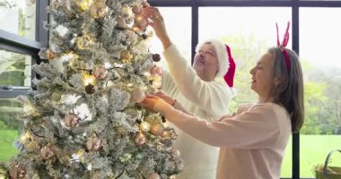 Noel ağacını mücevherlerle süsleyerek tatile hazırlanan çift, güneşlenme odasındaki ışıklar kucaklaşıyor. Şenlik, kutlama, samimiyet, mevsimlik, rahat, sıcak, neşe