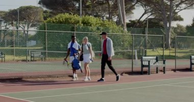 Kapıya uzanmak, farklı arkadaşların yürümesi, konuşması, sürgüyü açması, ısınmak için tenis kortuna girmesi. Aktif giysi, arkadaşlık, atletizm, açık hava, eğlence, canlı, takım çalışması.