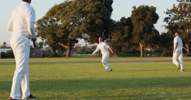 Kırmızı topu atan, çeşitli erkek kriket takım arkadaşları çimen tarlasında matkap talimi yapıyor, kopya uzayı. Atletik, takım çalışması, açık hava, sportmenlik, eğitim, rekabetçi, enerjik