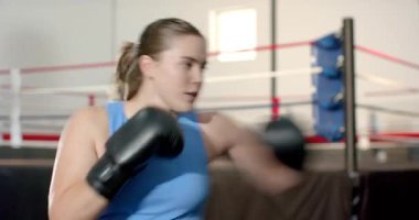 Antrenör olarak eldivenlerle boks yapan bayan sporcu ringe çıkıyor ve bilek hizasını gösteriyor. Martialarlar, koçluk, güç, eğitim, kararlılık, eylem, spor