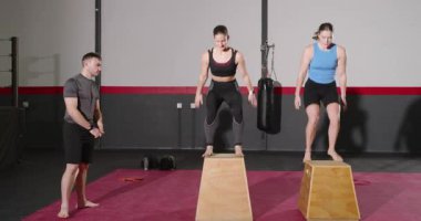 Erkek koç jimnastik salonunda atlama talimi, çömelme, zıplama, susuzluk, bitiş seti gibi şeyleri açıklıyor. Fitness, egzersiz, güç, eğitim, egzersiz, atletik, dinamik