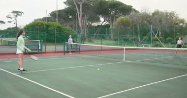 Besleyici, sahada yapılacak ralli için raket sallayan kadın arkadaşlara el altından top atıyor. Spor, eğlence, atletizm, takım çalışması, fitness, açık hava, dayanıklılık