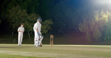 Bowler 'ın koşması, Hintli vurucunun sahne ışıkları altında topa karşı duruşunu değiştirdiğini gösteriyor. Spor, takım çalışması, yarışma, açık hava, gece, atletik, aksiyon