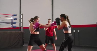 Koç bayan antrenörlere antrenman yaptırıyor kırmızı minderlerde boks eldivenleriyle, bacak korumalarıyla antrenman yapıyor. Spor, dövüş, atletizm, güçlendirme, eğitim, güç, disiplin