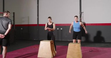 Antrenör kronometreyle işaret veriyor. Öğrenciler de kutunun üstünde zıplayıp kutu atlayışı yapıyor. Fitness, antrenman, atletizm, egzersiz, ısınma, güç, dayanıklılık