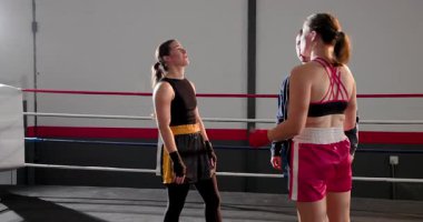 Dövüş talimatları veriyor, koç iki kadın boksöre kafa sallıyor, gülüyor, boks ringinde ısınıyor. Atletik, takım çalışması, akıl hocalığı, dinamik, disiplinli, enerjik, rekabetçi