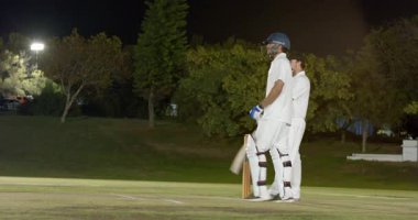 Çeşitli erkek çiftler vuruş vuruşu yapıyor, atış vuruşunu yapmadan önce işaret veriyor. Kriket, spor, gece, takım, aksiyon, yarışma, atletizm