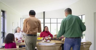 Çeşitli aileler yemek odasına ellerinde rosto tabakları ile girip bayram yemeği için mısır servis ediyorlar. Kutlama, kutlama, birliktelik, sıcaklık, neşe, sade, neşeli.