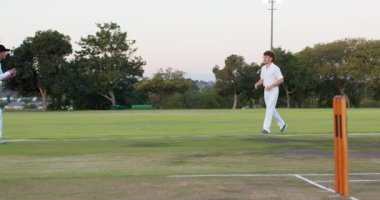 Beyaz erkek bovling oyuncusu sahada topu teslim ediyor. Sahada acı için bacağını kontrol ediyor. Atletizm, takım çalışması, spor, aktif, rekabet, açık hava, hareket