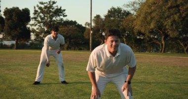 Koşu yapan erkek takım arkadaşları, kırmızı kriket topuyla bovling oynayıp parkta kutlama yapıyorlar. Atletizm, sportmenlik, açık hava, takım çalışması, eğlence, canlılık, rekabet