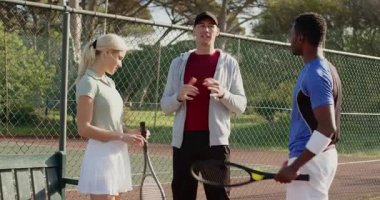 Koç topu atıyor, çeşitli gruplar tenis kortunda raket ve ayak egzersizi yapıyor. Atletik, antrenman, takım çalışması, profesyonel, canlı, performans, motivasyon