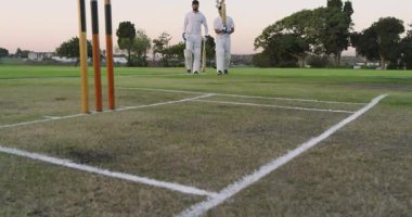 Kamera çeşitli takım arkadaşlarının sahaya çıkışına, yumruk tokuşturmasına, yarasaları fırlatmasına odaklanıyor. Kriket, takım arkadaşları, yoldaşlık, sportmenlik, açık hava, atletik, boş zaman