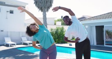 Orta yaşlı bir kadın ve Afro-Amerikalı bir adam sırayla havuz başında omuzlarını esnetiyorlar. Spor, açık hava, rahatlama, sağIık, çeviklik, egzersiz, boş zaman