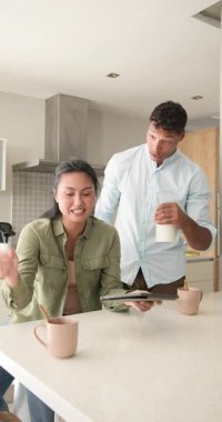 Tableti tıklattıktan sonra, çeşitli çiftler yemek tarifi izleyip mutfakta gülerek bardaklara süt döküyorlar. Yemek pişirme, kahvaltı, samimiyet, ev, iletişim, modern, dikey video