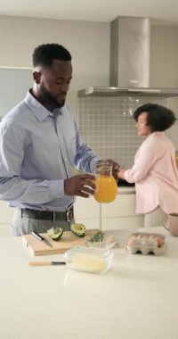 Dikey video: Çift modern mutfakta taze portakal suyunun tadını çıkarıyor, rahatlıyor. Yaşam tarzı, rahatlama, kahvaltı, içecek, sabah, içecek.