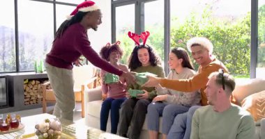 Çeşitli arkadaşlar Noel Baba şapkalı adamdan hediyeler alıyor ve oturma odasında selfie çekiyor. Kutlama, şenlik, sıcaklık, arkadaşlık, samimi, rahat, samimi