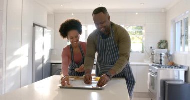 Çizgili önlük giyen, hamurdan topları pişirmek için mutfak tepsisine koyan çeşitli çiftler. Mutfak, takım çalışması, kırsal, aile dostu, modern, rahat, yaşam tarzı