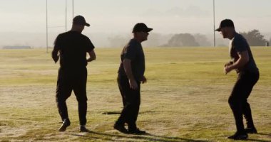 Kıdemli erkek takım arkadaşlarını duraklattıktan sonra çiğ sahada ayak antrenmanı için kale direkleriyle ayak sürüyorlar. Atletizm, takım çalışması, çeviklik, açık hava, fitness, gün doğumu, spor