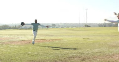 Koşan Afro-Amerikan adam, elmas kıvılcımlı takım arkadaşlarının kaskla tezahürat yaptığı kale levhasından geçiyor. Atletizm, takım çalışması, zafer, sportmenlik, açık hava, aktif, rekabetçi