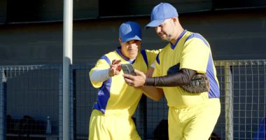 Erkek oyuncu kulübede kaydırıyor ve ekranı işaret ediyor, çeşitli erkek takım arkadaşlarını kalabalığa çekiyor. Sporcular, takım çalışması, yoldaşlık, boş zaman, açık hava, gündelik, genç işi.
