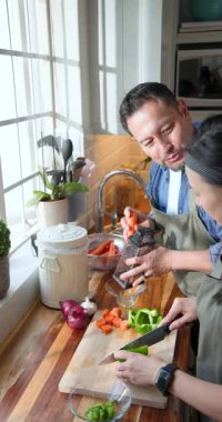 Dikey video: Yemek hazırlıklarına başlamak, mutfakta havuç rendelerken biber doğrayan Asyalı çift. Aşçılık, işbirliği, yerli, aşçılık, yaşam tarzı, hareketli, dikey video