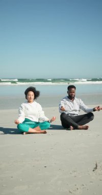 Dikey video: Sahilde meditasyon, çift okyanus dalgalarıyla huzurlu bir sabah geçiriyor. Meditasyon, rahatlama, sükunet, dinginlik, farkındalık, gündoğumu