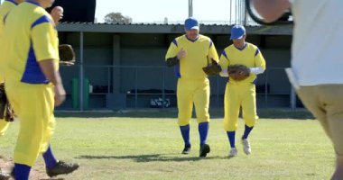 Gelişmekte olan erkek takım arkadaşları saha çimlerinde yürüyor, el sıkışıyor ve eldiven ve beysbol oynuyorlar. Sportmenlik, takım çalışması, yoldaşlık, atletizm, açık hava, rekabetçi, gündelik