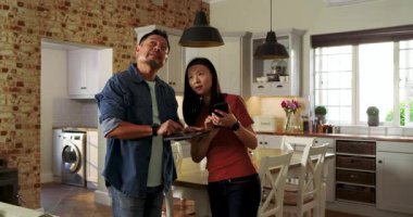 Tablet dinleme, Asyalı çift mutfaktaki kolye ışıklarını inceleyip seçenekleri onaylıyor. Teknoloji, modern, yaşam tarzı, iletişim, ev, etkileşim, aydınlanma