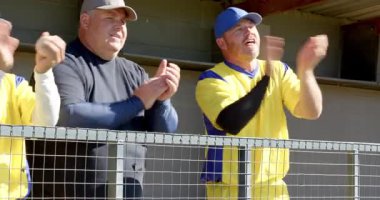 Yoğun oyuna tepki gösteren üniformalı erkek takım arkadaşları faul topu yakalıyor ve yedek kulübesinde kutlama yapıyorlar. Takım çalışması, yoldaşlık, sportmenlik, zafer, kutlama, açık hava, canlı