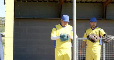 Yedek kulübesindeki erkek beyzbol takımı antrenör sinyaline eldiven alıp, koşup, sarılarak cevap veriyor. Sporcular, takım çalışması, sportmenlik, antrenman, rekabet, enerjik, enerjik