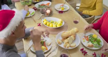 Noel Baba şapkalı Afrikalı Amerikalı adam tatil masasında ekmek yırtıyor, arkadaşları salata dağıtıyor, fotokopi çekiyor. Şenlik, kutlama, dostluk, sıcaklık, kırsal, açık hava, neşe