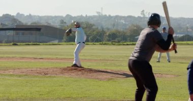 Atıcının ağırlığı değişiyor, dönüyor ve sahadaki vurucuya atışını yapıyor. Atletik, rekabet, takım çalışması, canlılık, açık hava, spor, strateji