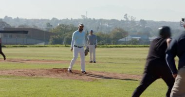 Hakem hazır olduğunu işaret ediyor, üst düzey erkek atıcı tümsekte, yakalayıcıya beyzbol topu teslim ediyor. Atletizm, spor, yarışma, açık hava, takım çalışması, aktif, yaz
