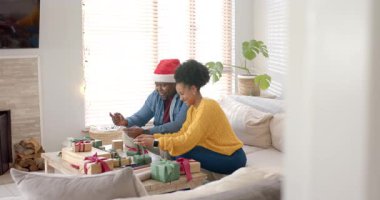 Hediye etiketini inceliyor, çeşitli çiftler evde birbirlerine gülümseyerek bayram hediyelerini paketliyor. Şen, samimi, etkileşim, kutlama, arkadaşlık, samimiyet, evcimen