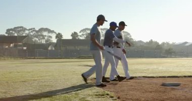 Şafak vakti beyzbol sopası ve eldiven taşıyan üç erkek takım arkadaşı ilk kaleye giriyor, defans yapıyorlar. Sporcular, takım çalışması, sportmenlik, antrenman, açık hava, canlı, sabahın erken saatlerinde