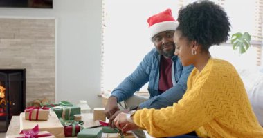 Kırmızı kurdele makarası alan, çeşitli çiftler kutlama için sehpaya bayram hediyelerini paketliyor. Şenlik, kutlama, samimiyet, sıcaklık, mevsimlik, dekorasyon, konforlu