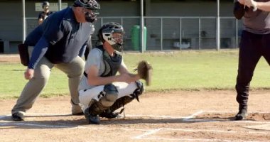 Atışı yakalıyor, erkek yakalayıcı miğferi atıyor ve oyuna devam etmek için dış sahaya yürüyor. Atletizm, spor, takım çalışması, açık hava, rekabet, aksiyon, eğlence