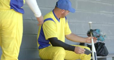 Takım arkadaşı sohbete giriyor, formalı takım arkadaşları spor çantasındaki telefonları inceliyor. Sporcular, işbirliği, iletişim, günlük, takım çalışması, modern, spor kıyafetleri