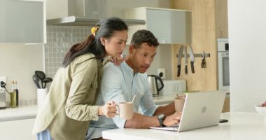 Çeşitli çiftler omuzlarına dokunuyor, kahvelerini yudumluyor, mutfak adasında dizüstü bilgisayarlarıyla iş birliği yapıyorlar. İşbirliği, samimiyet, sabah rutini, modern mutfak, çalışma alanı, bağlantı, yaşam tarzı