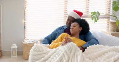 Noel Baba şapkalı Afro-Amerikan çift, sıcak bir hava için kanepede örgü örüyorlar. Romantizm, samimiyet, rahatlık, rahatlık, ev, konfor, şefkat