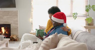 Farklı çiftler evdeki kanepeye kadın hediye kutusundaki adamı kurdele açma hediyesini çözerken koyuyor. Romantizm, samimiyet, sıcaklık, kutlama, rahatlık, ev, sevgi